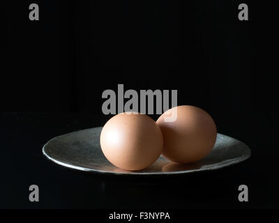 Two brown eggs on a plate, dark. Stock Photo