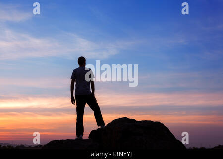 Silhouette of a man with raised-up arms at the beautiful sunset on the mountain. Background Stock Photo