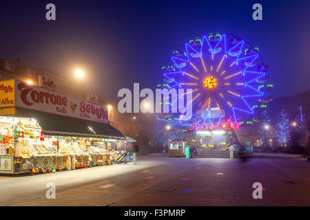 Illuminated observation wheel and mobile stall with sweets on town square of Alba, Italy. Stock Photo