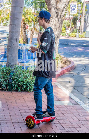 A teen checks his smartphone as he balances on an electric powered scooter board in Santa Barbara, California. Stock Photo