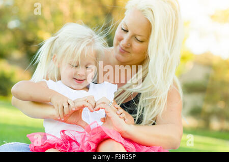 Cute Little Girl With Mother Making Heart Shape with Hands Outdoors. Stock Photo