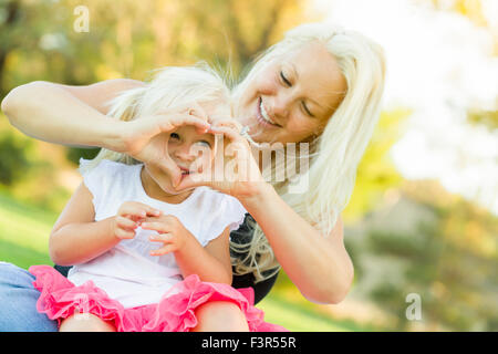 Cute Little Girl With Mother Making Heart Shape with Hands Outdoors. Stock Photo