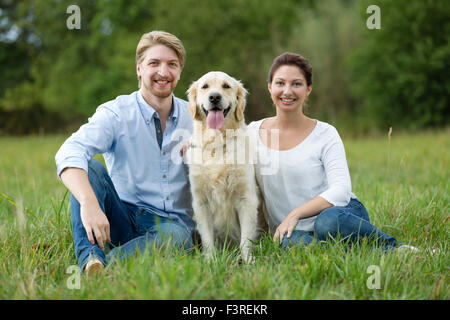 Couple sitting on meadow with Labrador Stock Photo