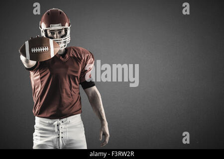 Composite image of portrait of american football player showing football to camera Stock Photo