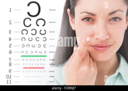 Composite image of brunette holding contact lens and smiling at camera Stock Photo