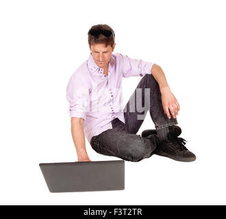 A handsome young businessman sitting on the floor, working on his laptop, isolated for white background. Stock Photo