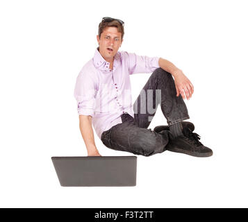 A young man sitting on the floor looking on his computer and is very surprised, isolated for white background. Stock Photo
