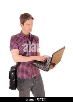 A young man standing isolated for white background holding his laptop and working on with his briefcase over his shoulder. Stock Photo