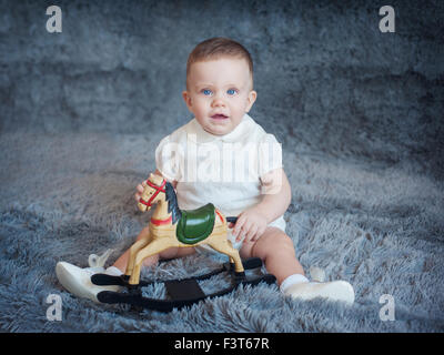 Cute boy on a gray background with a toy horse in his hands Stock Photo