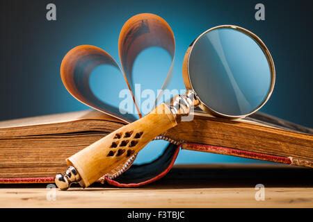 old book and magnifying glass on wooden table and blue background Stock Photo