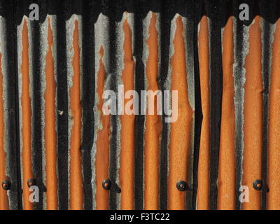 strong sunlight on rusty overlapping galvanised corrugated sheet metal with fixings creating striking shadow pattern Stock Photo