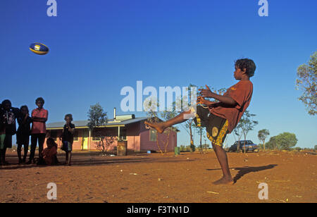 ABORIGINAL BOY A KICKING BALL, YUELAMU (MOUNT ALLAN) IN THE NORTHERN TERRITORY, AUSTRALIA Stock Photo