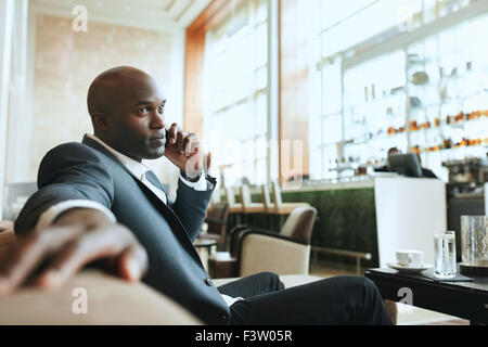 African business man talking on mobile phone while waiting in a hotel lobby. Young business executive using cell phone while wai Stock Photo