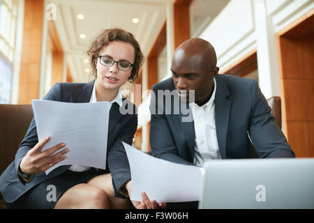 Portrait of young business man and woman sitting in cafe and discussing contract. Diverse businesspeople meeting in hotel lobby Stock Photo