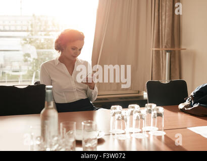 Portrait of young businesswoman sitting in business conference room using mobile phone. Female executive sitting in hotel confer Stock Photo