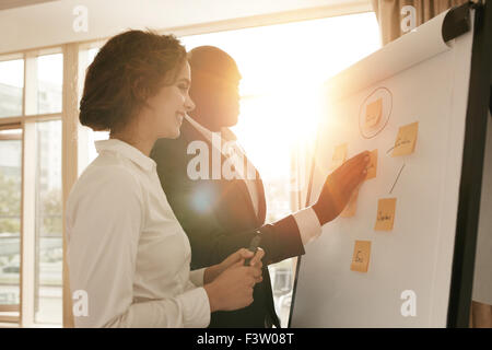 Two business colleagues working on project together. Business people putting their ideas on whiteboard during a presentation in Stock Photo