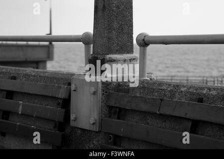 Black and white image of Deal Pier with the english channel in the background, focussing on a metal bracket and cement lamp post Stock Photo