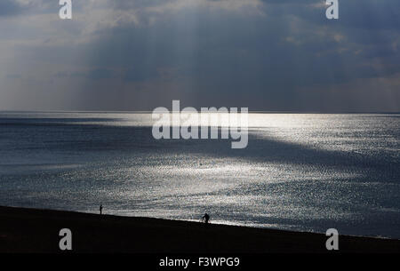 Brighton, UK. 13th October, 2015. A man pushes his bicycle along the beach as shafts of sunlight break through  the dark clouds which are forming off Brighton today The weather is set to become more unsettled over the next few days  Credit:  Simon Dack/Alamy Live News Stock Photo