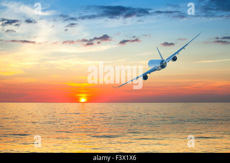 Jumbo jet airplane flying above tropical sea at beautiful sunset. Stock Photo