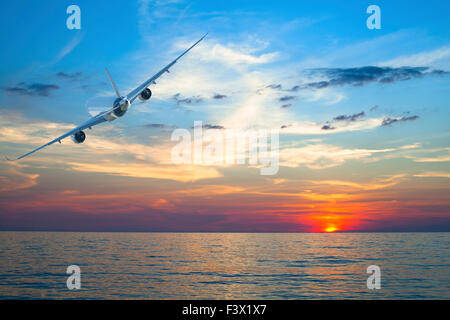 Airplane flying above tropical sea at amazing sunset. Stock Photo