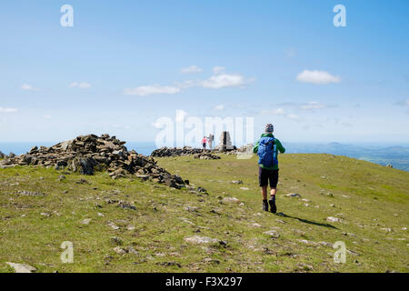 Hikers approaching trig point cairn on Moel Hebog mountain summit in mountains of Snowdonia National Park, North Wales, UK Stock Photo