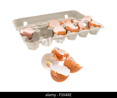 A group of broken and used eggs in the foreground with the remainder in a cardboard carton in the background. Stock Photo