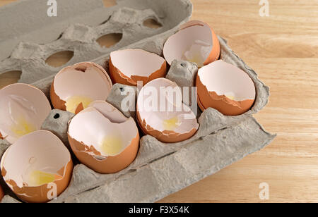 A carton of broken and used eggshells on a wood counter top illuminated with natural light. Stock Photo