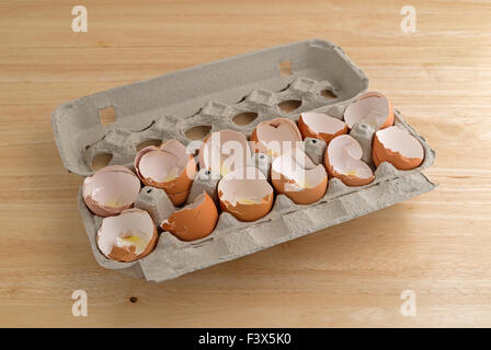A dozen broken eggshells in an opened cardboard container on a wood counter top illuminated with natural light. Stock Photo