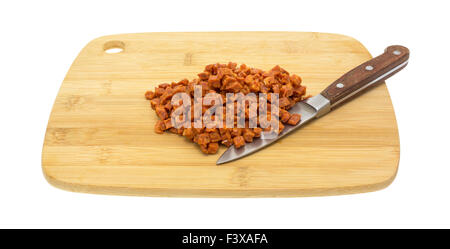 Pepperoni pizza topping that has been chopped into small cubes on a wood cutting board with a kitchen knife isolated on a white Stock Photo