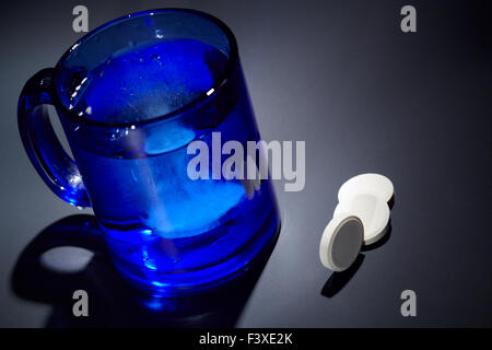 Tablet dissolving in a blue glass of water. Stock Photo