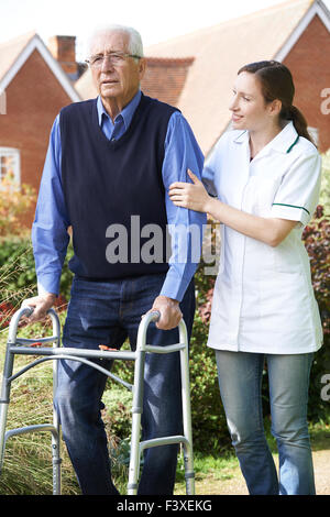 Carer Helping Senior Man To Walk In Garden Using Walking Frame Stock Photo