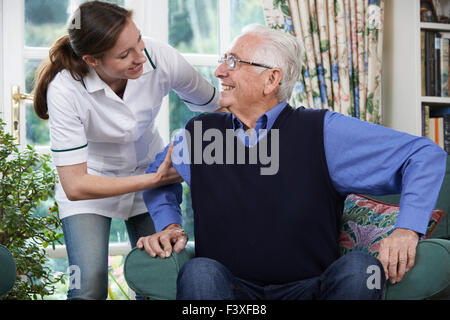 Care Worker Helping Senior Man To Get Up Out Of Chair Stock Photo