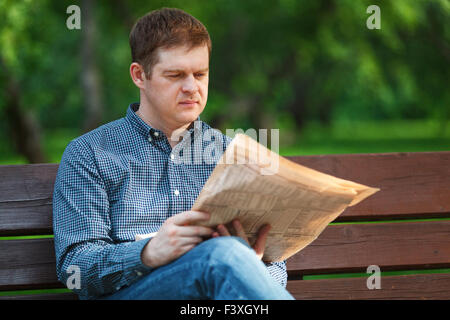 Man reads newspaper on bench in the park Stock Photo