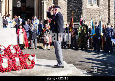 Remembrance Sunday at Ramsgate. Senior veteran soldier salutes the war memorial having laid a poppy wreath. Background, soldiers holding banners. Stock Photo