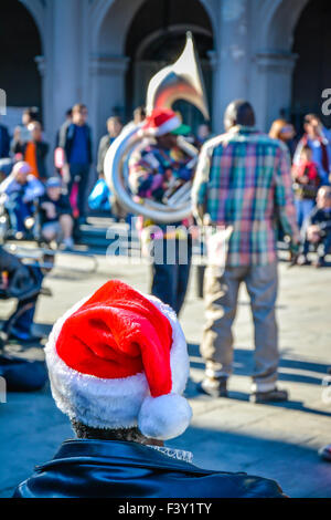 Rear view of man wearing Santa hat enjoying entertainment by street musicians, Jackson Square, French Quarter, New Orleans, LA Stock Photo