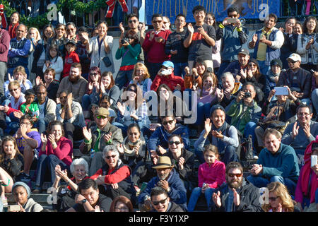 Crowd of ethnically diverse people of all ages, in the USA, some sitting,  some standing while laughing & applauding while watching performance art. Stock Photo