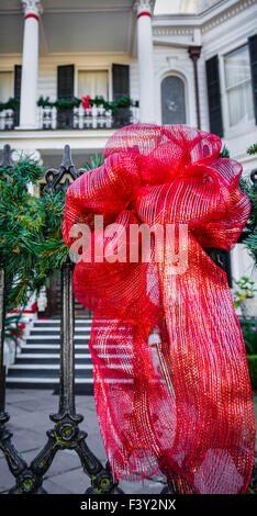 Red ribbon tied around black wrought iron fence in front of historical colonial home in the Garden District in New Orleans, LA Stock Photo