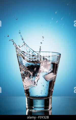 Ice cube splashing into a glassl of water. Blue background Stock Photo ...