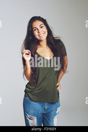 Lovely attractive young woman with a warm friendly smile wearing ragged designer jeans and a casual t-shirt standing looking at