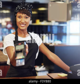 Young shop owner requesting payment holding out a handheld banking machine for a customer to enter the code for their credit car Stock Photo