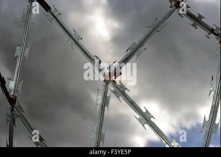 A shiny barbed razor wire fence photographed against a dramatic stormy sky. Stock Photo