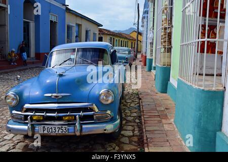quiet colourful street in Trinidad Cuba with a couple of local guys hanging out and parked vintage cars Stock Photo