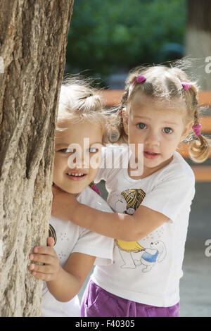 Two children peep out from behind a tree Stock Photo