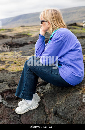 Female tourist seated on lava rocks along coast, Hawai'i Volcanoes National Park, Big Island, Hawai'i, USA Stock Photo