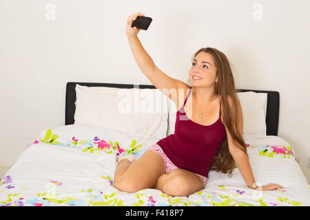young woman taking a selfie with her phone in her bedroom Stock Photo