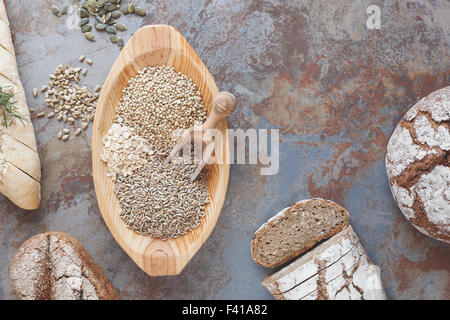 Bread and different seeds and grains on table and in rustic wooden dough bowl top view, vintage style Stock Photo