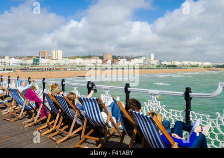 People sitting in deckchairs on Brighton Pier overlooking the sea and Brighton Beach. East Sussex, England. Stock Photo