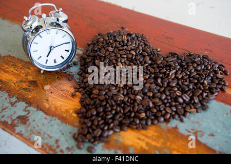 alarm clock and heart shape of coffee beans on wooden vintage table Stock Photo