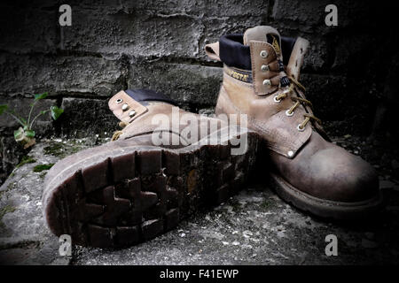 very old worn out rigger boots working steel toe capped outside against wall England Stock Photo