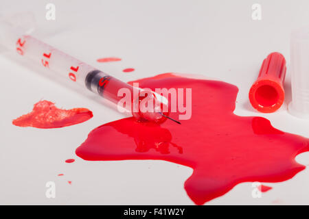 High Angle View of Syringe Needle Squirting Red Liquid or Blood onto White Background in Studio Still Life - Concept Image Stock Photo